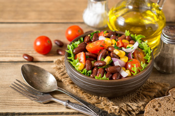 Fresh vegetable salad with beans in ceramic bowl on wooden table.