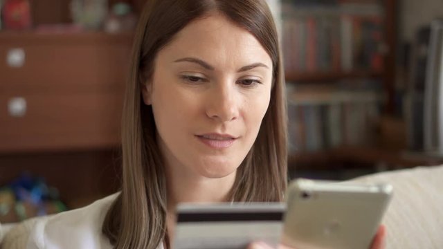 Slow Motion Woman in white blouse sitting on sofa in living room buying online with credit card on smartphone