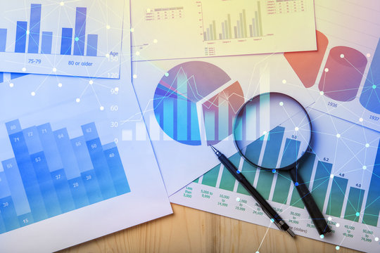 Magnifying glass and documents with analytics data lying on table,selective focus
