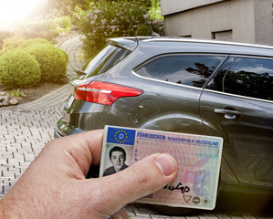 Führerschein in der Hand vor einem Auto