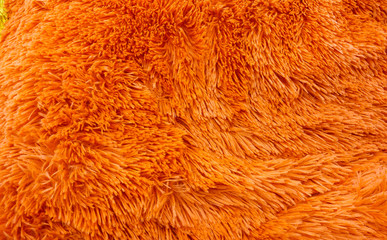 Fluffy texture fabric. Closeup of the pillow with orange fur cover. Abstract background.
