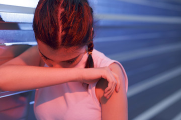 Beautiful girl feeling head pain, stress and disorientation. Holding her hands near her face. Outdoors, leaning on a steel wall. Taken using blue and red flashes.