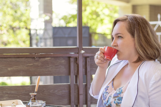 Young business lady drinking coffee in the street cafe. Coffee and cakes on the table. Sunny day. Coloring and processing photos. Shallow depth of field.