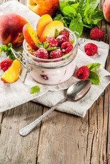Summer healthy breakfast. Overnight oatmeal in a jar, granola, nuts, fresh raspberries and peach, decorated with mint leaves. On the old rustic wooden table. Copy space