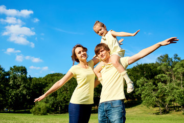 Fototapeta premium Happy family smiling in the park. Mother, father and daughter in nature on background of blue sky and trees.