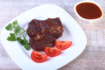 Grilled beef steak with tomato, and hot asian chillies garlic sauce on plate on wooden background.