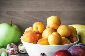 Fresh apricots in a white dish and other fruits on the kitchen table.Healthy lifestyle