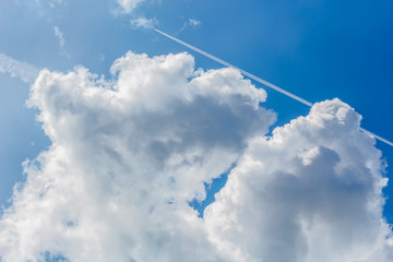 Blue sky with cumulus clouds and contrails, close-up