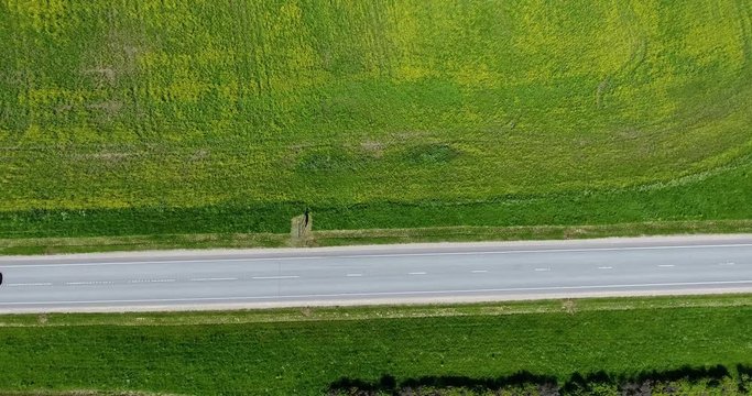 Camera moving down on the asphalt highway passing amount green pastures. Bus overtaking car. Top view