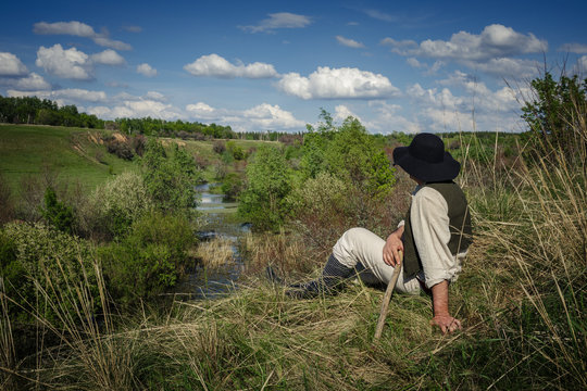 man sits on a hill near the river