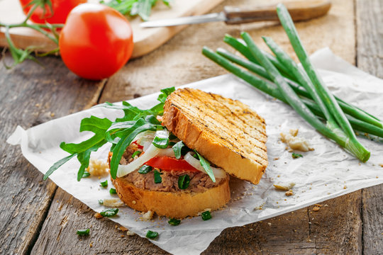 Toast sandwich with tuna, tomato, onion and arugula. Traditional healthy food made of fish, vegetables and grilled bread.