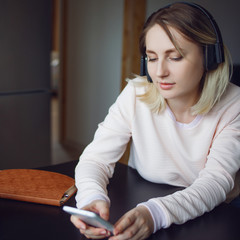 Young blond woman with mobile phone and headphones, listen online courses