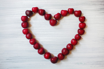 Heart made of dark cherries. Red fruit on wooden background. Summer sends love. Particles of art.