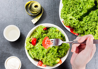 Hand with fork over white ceramic bowl of delicious salad of cucumbers and tomatoes and vegetables on the kitchen table.