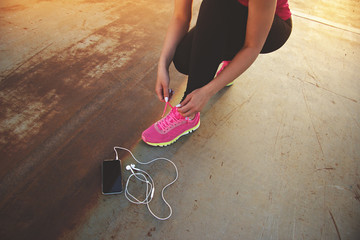 Tying her shoelaces. Cropped image of young and beautiful sporty woman tying shoelaces on the bridge. Smart phone with headphones are nearby.