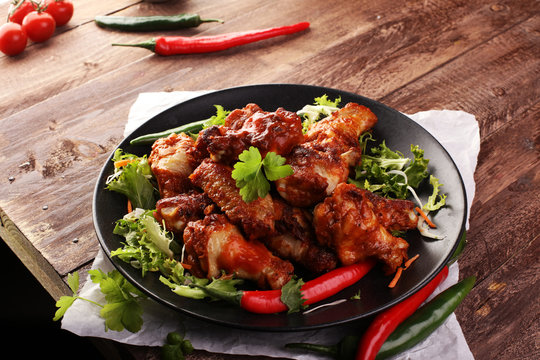 barbecue chicken wings close up on wooden tray with red spice sauce and salad