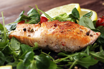 baked salmon grilled pepper lemon on a plate with lettuce leaves and tomato on wood background - healthy eating concept