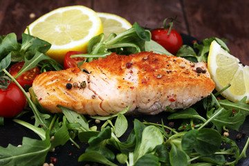 baked salmon grilled pepper lemon on a plate with lettuce leaves and tomato on wood background - healthy eating concept