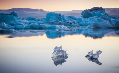 Two small pieces of ice flowing and reflecting in cold lake with a big icebergs behind, jokulsarlon glacier lagoon, Iceland