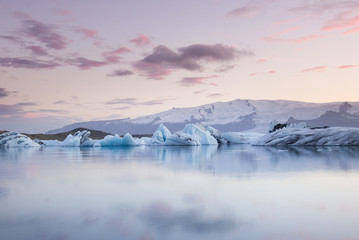 Giant pieces of ice flowing on and reflecting in cold lake with a huge glaciar behind, jokulsarlon...