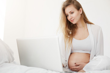 Young pregnant woman browsing an online store searching for toddler clothes