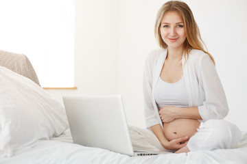 Pregnant woman using laptop at home. Online entrepreneur running her online store for kids apparel
