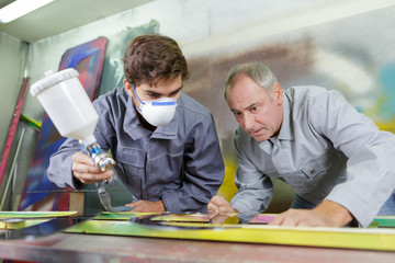 young painter using spray gun under master surveillance