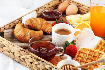 breakfast in bed with fruits and pastries on a tray -waffles, croissants, coffe and juice