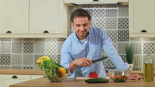 Portrait of attractive young man possing with knife and smiling on the camera in the kitchen.