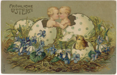 Two babies and a chick hatching out of Easter eggs. Date: circa 1910