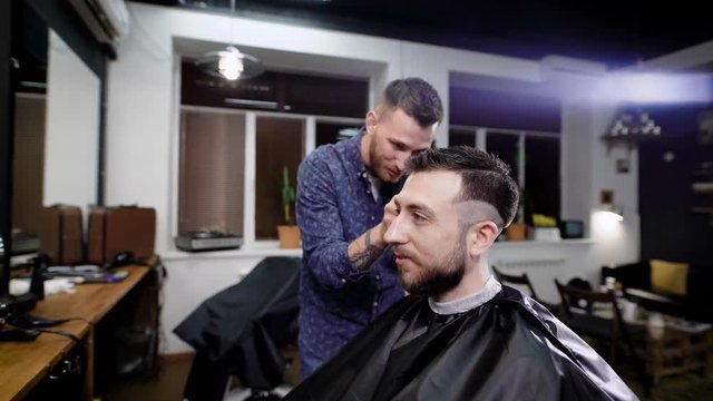 A young man came to barbershop in order to get a stylish haircut and fashionable styling from a professional hairdresser