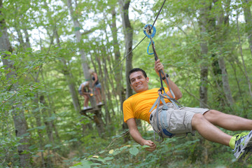 Naklejka na ściany i meble smiling man riding a zip line in the forest