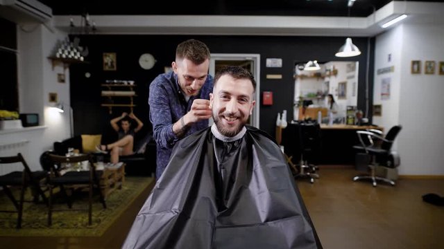 A stylish hairdresser talks to a beauty salon visitor who came to get uqdaku and refresh a haircut in barbershop, the visitor is happy