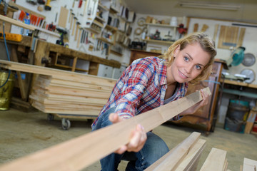 happy female carpenter holding wooden plank
