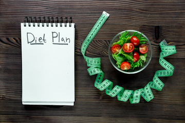 Notebook for diet plan, salad and measuring tape on wooden table top view mock up