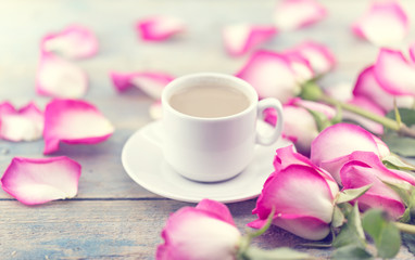 Fototapeta na wymiar Cup of coffee on rustic wooden table in a frame of pink roses. Greeting card with flower. Soft focus.