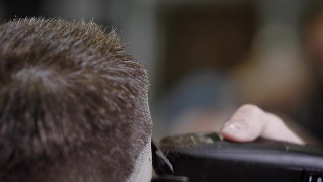 A close shot at the process of trimming hair with a hair clipper, the hairdresser uses a comb to help create a hairstyle