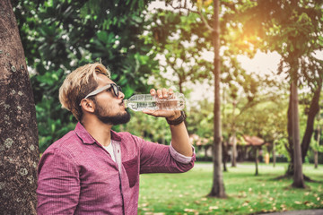 Fototapeta premium Young Hipster Man Drinking Water from Bottle after Traveling in Summer - Lifestyle Concept