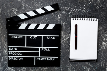 Work table of producer. Movie clapperboard and notebook on grey stone background top view