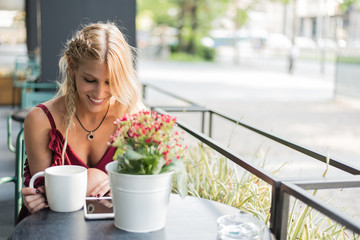 Happy blonde beautiful woman using a mobile phone drinking a cup of coffee in a terrace