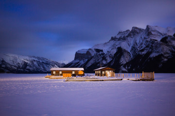 Empty boat dock on frozen lake covered by snow in high mountains during night Lake Minewanka, Banff national park, Canada