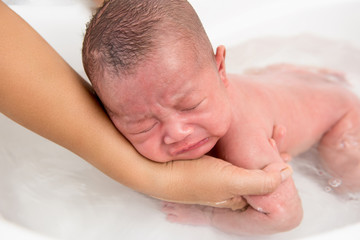 Fototapeta na wymiar Little newborn baby crying while being taken a bath
