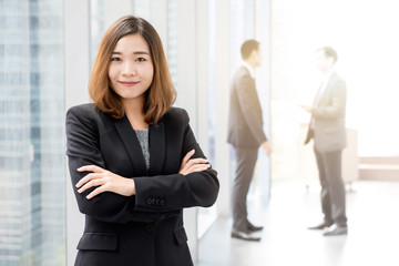 Asian businesswoman standing and crossing her arms in office building hallway