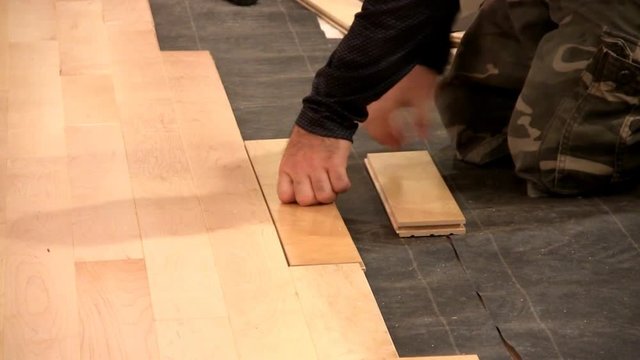 Floor installer gets on hands and knees to and taps piece of flooring tightly in place