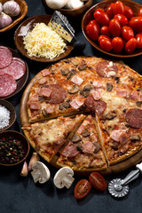 pizza with salami and ingredients on a black background, top view, vertical