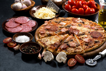 pizza with salami and ingredients on a black background