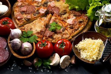 pizza with sausage and cheese and ingredients on a black background, closeup