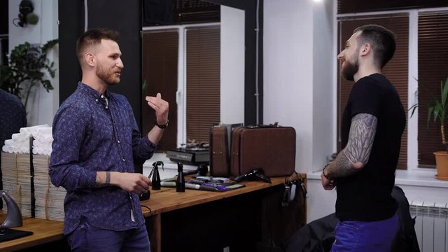 A young hair stylist who works in a barbershop communicates with the client in a friendly way, who has come to the ritual beauty salon for men