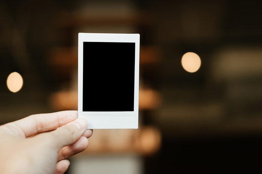 front view. hand of young woman holding blank Polaroid film. have blur interior cafe are background. image for abstract,body part,camera,equipment concept