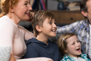 Closeup Of Happy Smiling Family Sitting On Couch Watching TV, Parents Spending Time With Children In Living Room